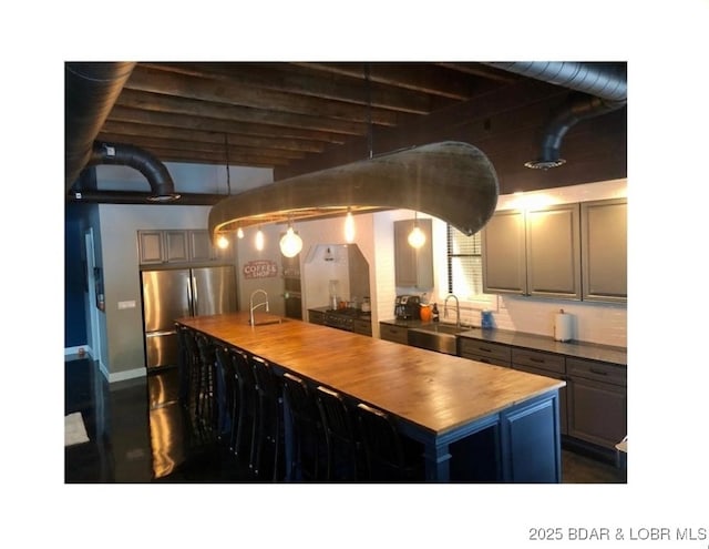 kitchen featuring a sink, an island with sink, freestanding refrigerator, and butcher block countertops