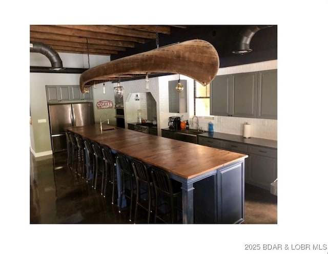 kitchen with butcher block counters, freestanding refrigerator, gray cabinetry, and a sink