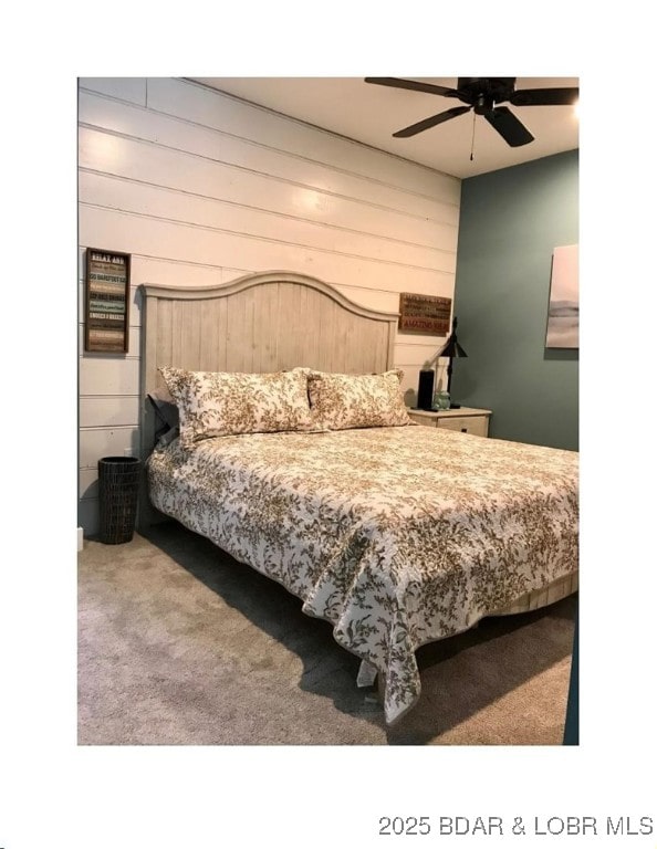 bedroom with carpet flooring, ceiling fan, and wooden walls