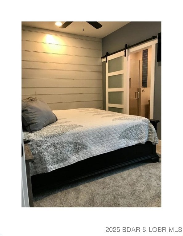 bedroom with ensuite bathroom, a ceiling fan, a barn door, wooden walls, and carpet flooring