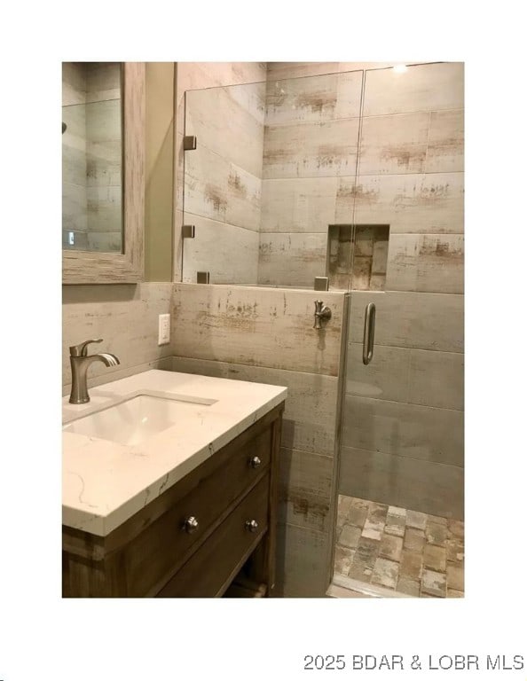 full bath featuring tasteful backsplash, tile walls, a stall shower, and vanity