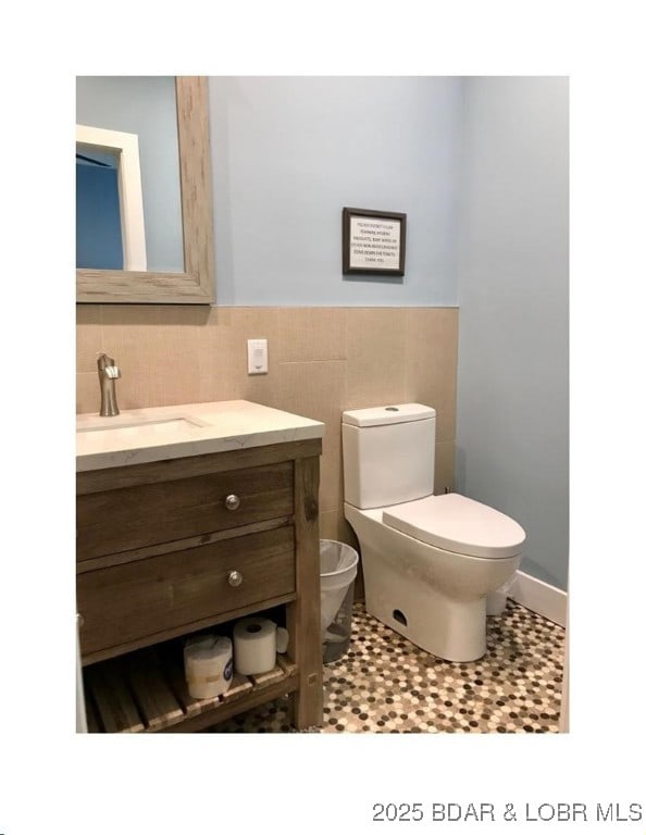 bathroom featuring toilet, tile walls, wainscoting, and vanity