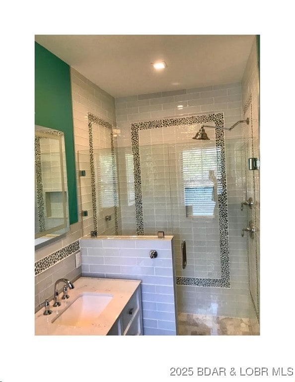 bathroom featuring tasteful backsplash, a shower stall, vanity, and tile walls