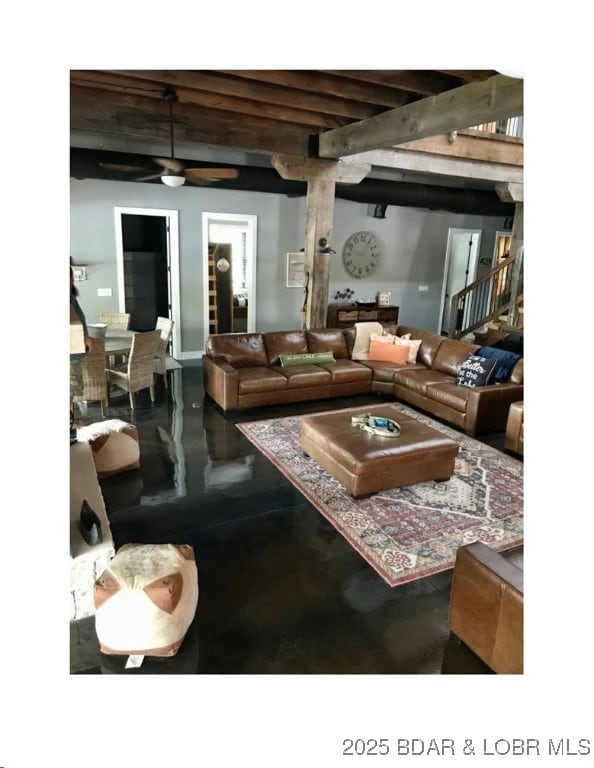 living room with beamed ceiling, a ceiling fan, and concrete flooring