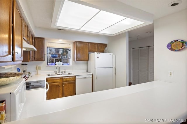 kitchen with a sink, white appliances, a peninsula, brown cabinetry, and light countertops