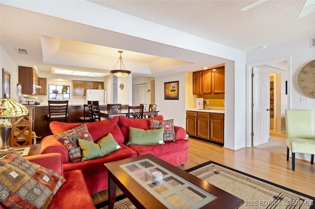 living area featuring visible vents, light wood-style flooring, a textured ceiling, and a raised ceiling