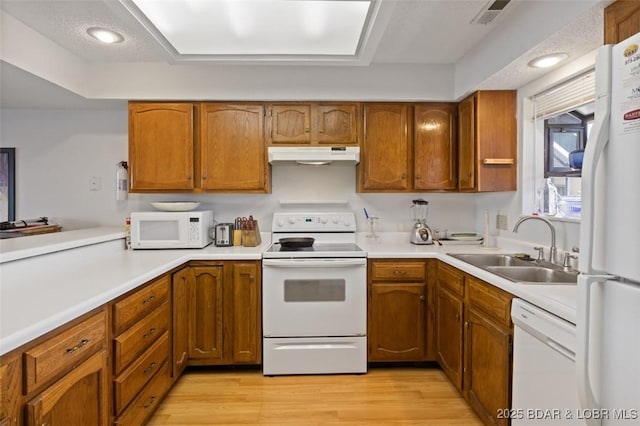 kitchen featuring white appliances, brown cabinetry, a sink, under cabinet range hood, and light wood-type flooring