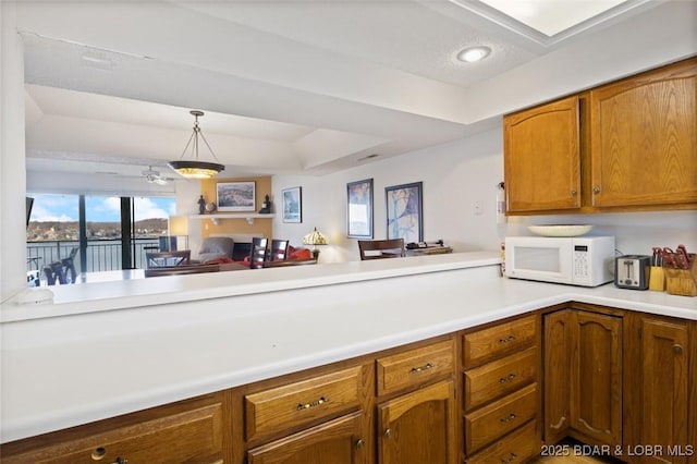 kitchen with white microwave, hanging light fixtures, brown cabinets, and light countertops