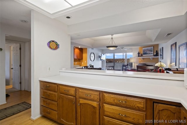 kitchen featuring a tray ceiling, brown cabinets, light wood-style floors, and visible vents