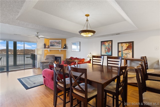 dining space featuring ceiling fan, wood finished floors, a glass covered fireplace, a textured ceiling, and a raised ceiling