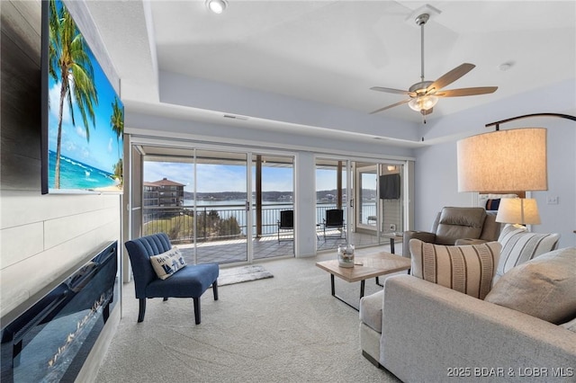 living area with ceiling fan, a tray ceiling, carpet, and a water view