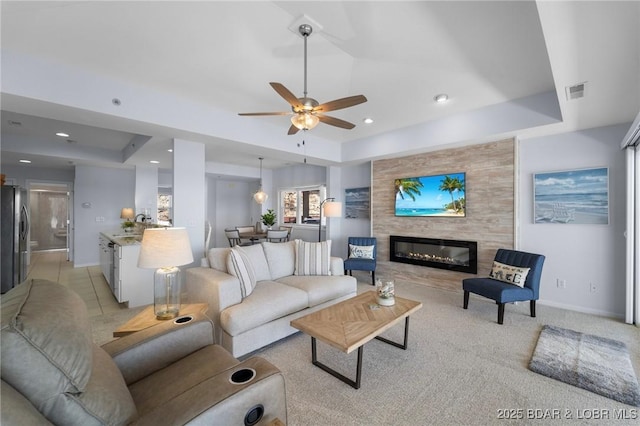 living room with a tray ceiling, a large fireplace, visible vents, and ceiling fan