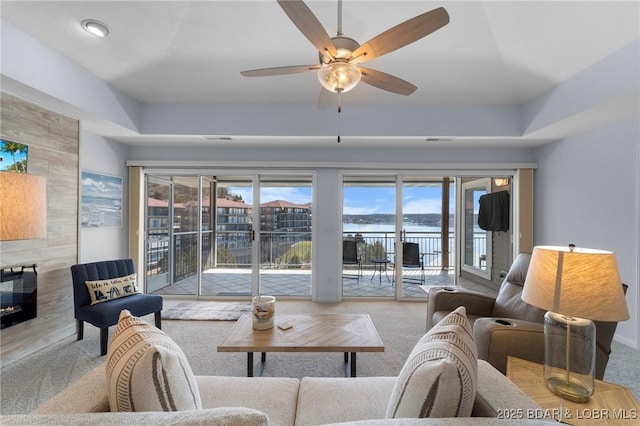 living area featuring a raised ceiling, carpet, ceiling fan, and a fireplace