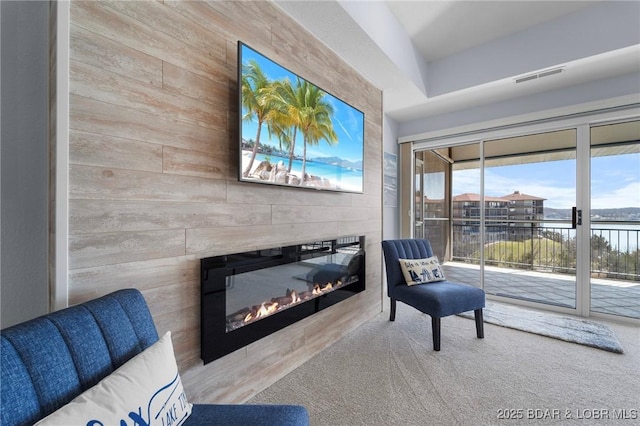 sitting room with a glass covered fireplace, wood walls, and visible vents