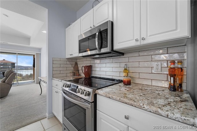 kitchen with backsplash, white cabinetry, stainless steel appliances, light stone countertops, and light colored carpet