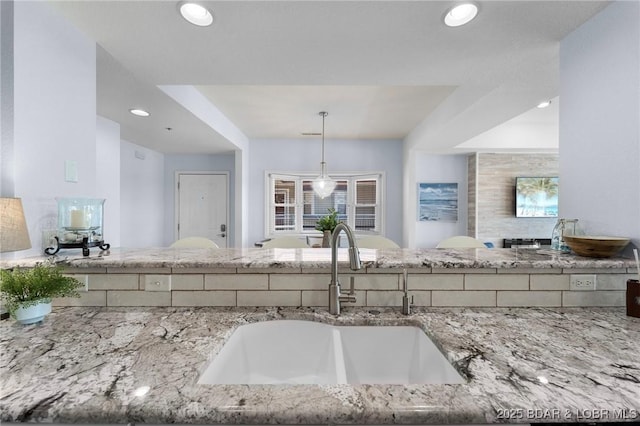 kitchen with decorative light fixtures, stone counters, recessed lighting, and a sink