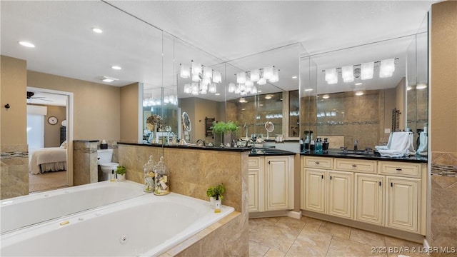 bathroom with a ceiling fan, ensuite bathroom, a tub with jets, tile walls, and vanity