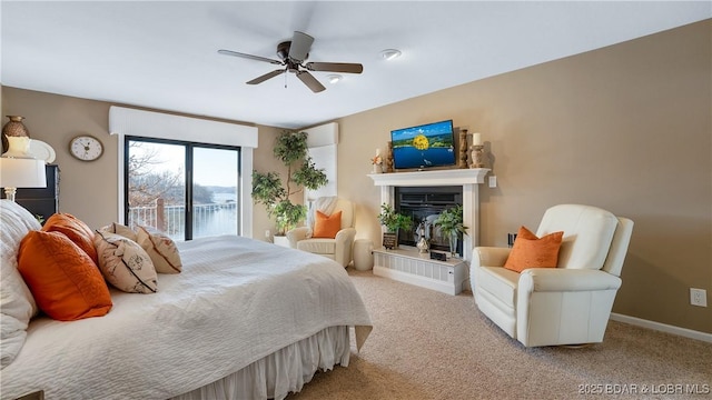 bedroom featuring a glass covered fireplace, baseboards, carpet floors, and ceiling fan