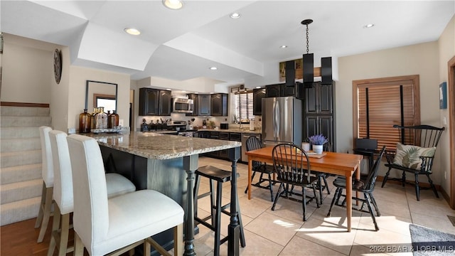 kitchen with light tile patterned floors, light stone countertops, recessed lighting, stainless steel appliances, and a kitchen breakfast bar