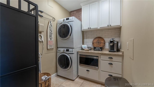 laundry room featuring light tile patterned flooring, cabinet space, and stacked washer and clothes dryer