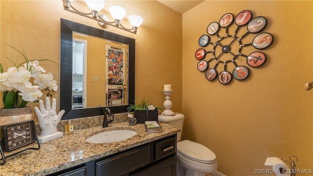 half bath with toilet, vanity, and a textured wall