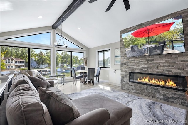 living area with baseboards, lofted ceiling with beams, ceiling fan with notable chandelier, a fireplace, and wood finished floors