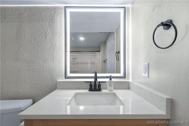 full bathroom featuring toilet, vanity, and a textured wall