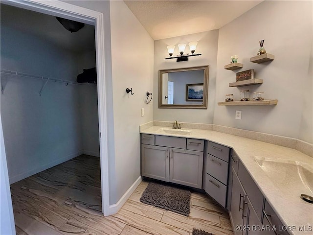 full bathroom with vanity, a walk in closet, and baseboards