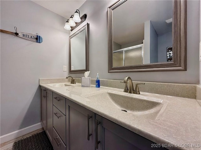 bathroom featuring double vanity, baseboards, a shower with door, and a sink