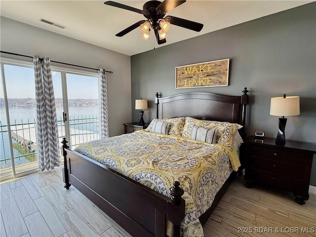 bedroom featuring a ceiling fan, wood finished floors, visible vents, a water view, and access to outside