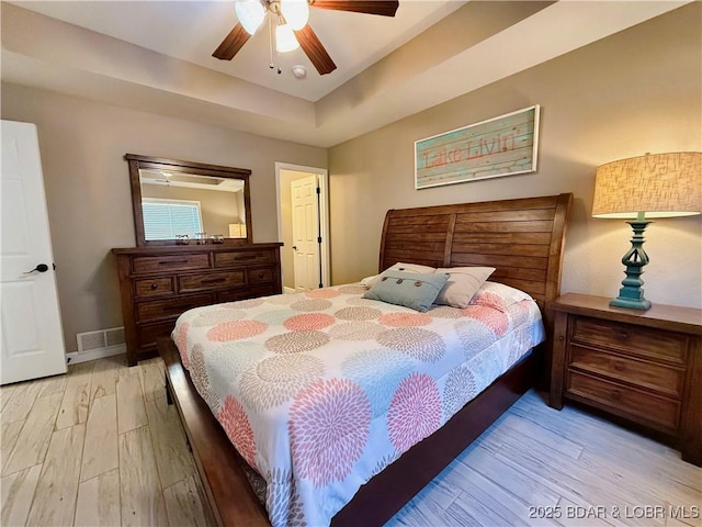 bedroom featuring baseboards, visible vents, a tray ceiling, ceiling fan, and light wood-style floors