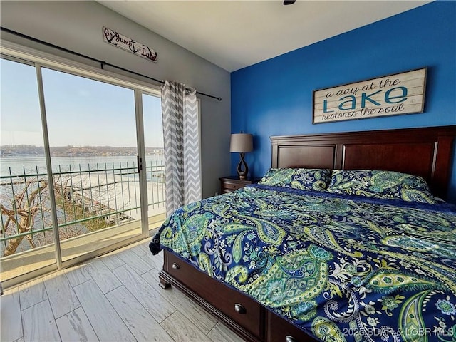 bedroom featuring access to exterior, wood finished floors, and a water view