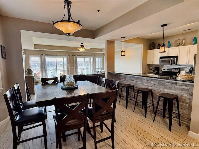 dining space with a raised ceiling, baseboards, light wood finished floors, and ceiling fan