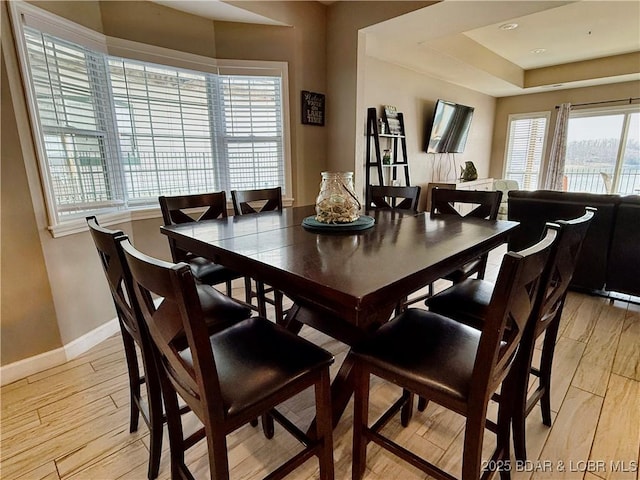 dining area with light wood-style flooring, a raised ceiling, and baseboards