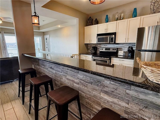 kitchen featuring light wood-style flooring, stainless steel appliances, white cabinetry, tasteful backsplash, and a kitchen bar