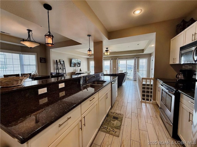 kitchen featuring light wood finished floors, a sink, appliances with stainless steel finishes, a raised ceiling, and open floor plan