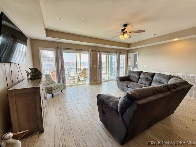 living room with light wood finished floors, ceiling fan, and a tray ceiling