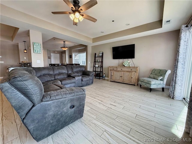 living area featuring a ceiling fan, baseboards, visible vents, a raised ceiling, and light wood-type flooring