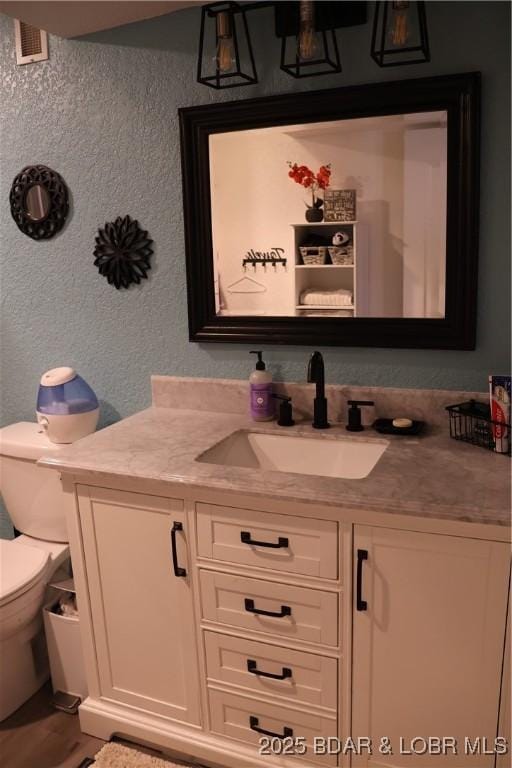 half bath featuring toilet, vanity, and a textured wall