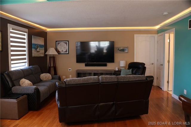 living area with baseboards, wood finished floors, visible vents, and ornamental molding