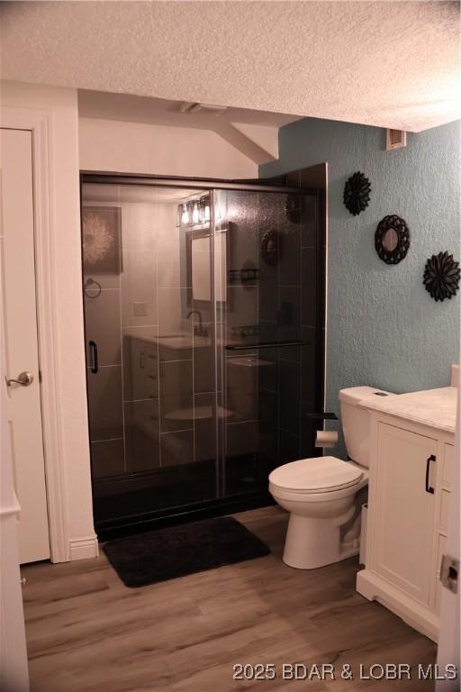 full bath featuring a shower stall, toilet, wood finished floors, a textured wall, and a textured ceiling