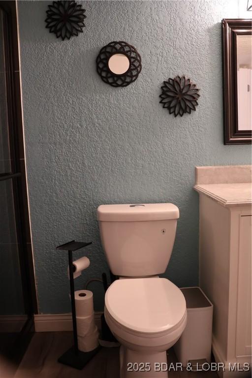 bathroom featuring a shower with door, toilet, and a textured wall