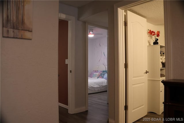 hall featuring baseboards, a textured ceiling, dark wood finished floors, and a textured wall