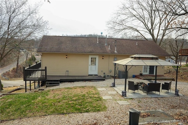 rear view of property with a deck, a patio, and a shingled roof