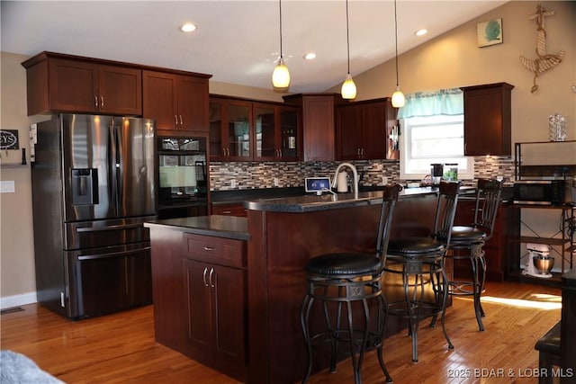 kitchen with wood finished floors, a kitchen breakfast bar, stainless steel refrigerator with ice dispenser, dark countertops, and black oven