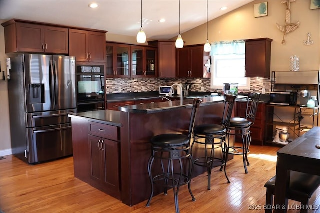 kitchen with dark countertops, tasteful backsplash, stainless steel appliances, light wood finished floors, and vaulted ceiling