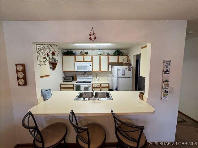 kitchen featuring a sink, a kitchen breakfast bar, white appliances, a peninsula, and light countertops