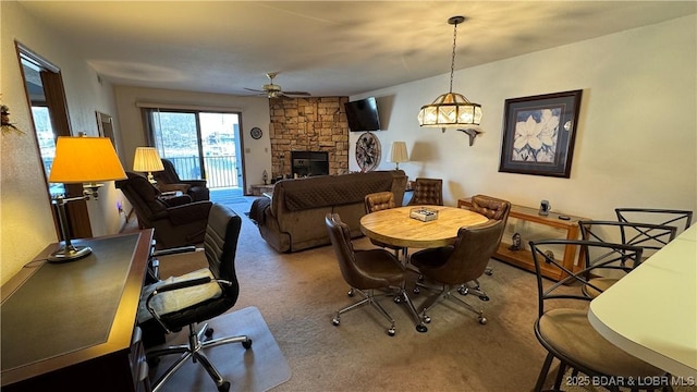 dining space with carpet, a stone fireplace, and a ceiling fan