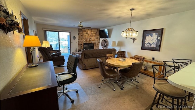 carpeted dining room featuring a stone fireplace and ceiling fan