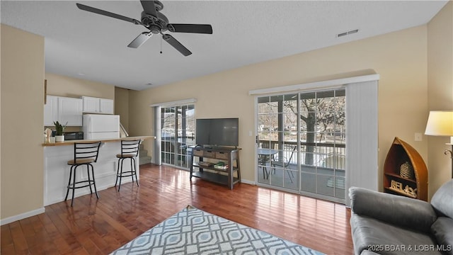 living area featuring visible vents, baseboards, a ceiling fan, and wood finished floors